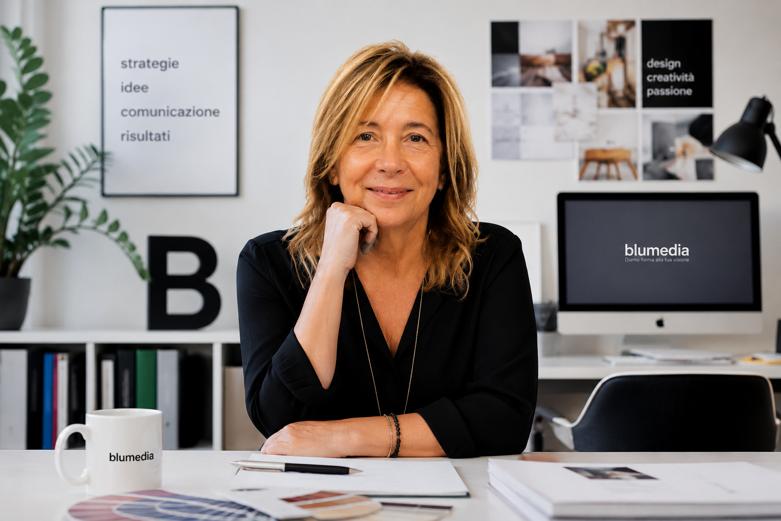 Professional woman in a black blouse sits at a desk, smiling at the camera, with blumedia branding in the workspace behind her